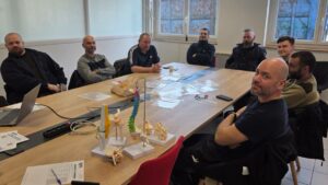 Groupe d'employés de PRIVÉ SA en formation Gestes et Postures avec Ignaxis, autour d'une table avec modèles anatomiques de colonne vertébrale et articulations.
